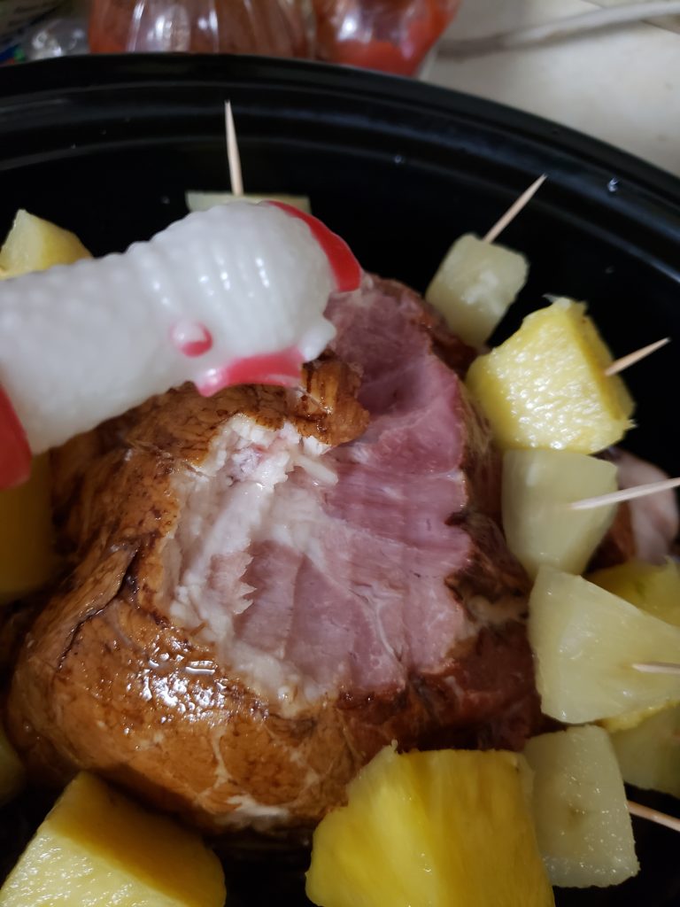 Chick-o, my rubber chicken is looking at the butt end of a ham, that is missing a slice, which is surrounded by pineapple chunks toothpicked to the ham and in the crockpot.